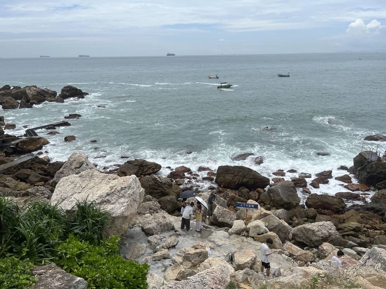 从山顶下降至西涌山脚下,俯瞰布满礁石的海岸;近岸浪花在岩石间翻涌,海面有数艘小船,远处地平线附近可见多艘船只